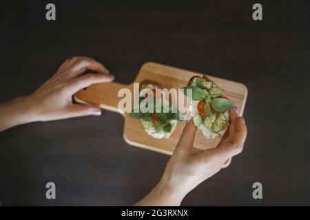 Female hand holding toast with avocado, cherry tomatoes and basil Stock Photo
