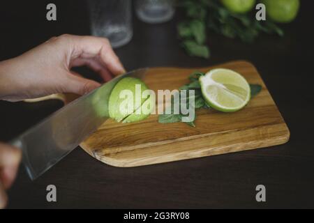 Crop of hand, knife and sliced lime on the wooden board Stock Photo