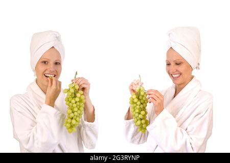 two young women in white bathrobes eating grapes Stock Photo