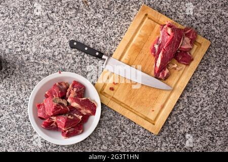 Diced, fresh red meat on a deep dish and kitchen knife over a wooden cutting board. Top-down view. Stock Photo