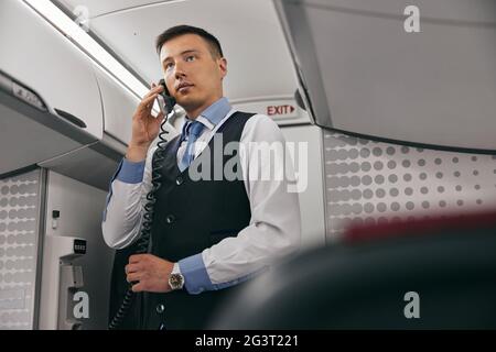 Flight attendant talk on board phone in airplane Stock Photo