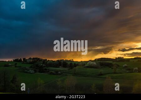 Dramatic cloudy sky at sunset over hilly grass covered landscape in Eifel, Germany Stock Photo