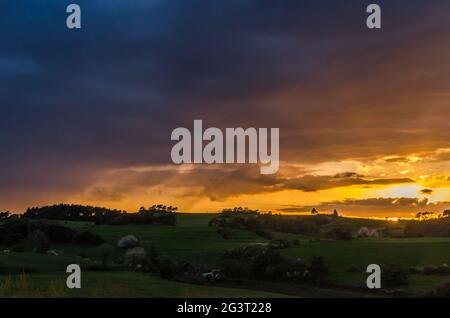 Dramatic cloudy sky at sunset over hilly grass covered landscape in Eifel, Germany Stock Photo