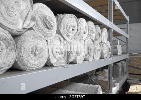 White material in rolls is on the shelves of the warehouse. Covering material. Textiles for the production of rags. Stock Photo