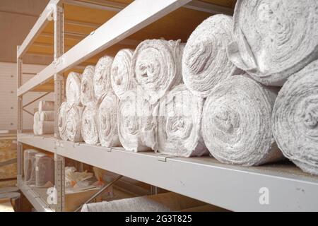 White material in rolls is on the shelves of the warehouse. Covering material. Textiles for the production of rags. Stock Photo