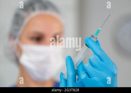 Experienced masked nurse prepared a syringe for injection, filling it with medicine Stock Photo