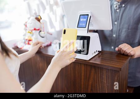 cashier using digital device for payment. Man waiter calculates young woman in cafe by mobile phone via QR code of Alipay or Wechat pay (popular Stock Photo