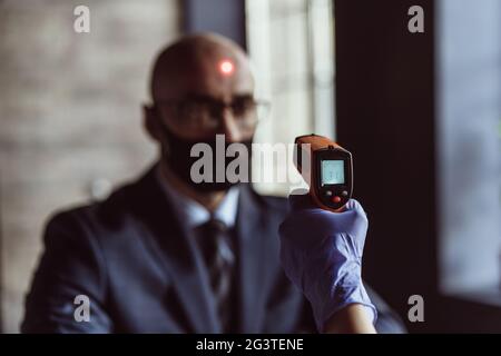 Health officer checking temperature of a businessman in the entrance of the business center. Businessman must go through fever m Stock Photo