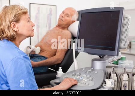 Female technician diagnosing male patient using modern ultrasound scanner in private clinic Stock Photo