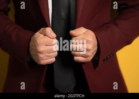 Close up on hands holding a business man burgundy jacket with two hands fixing it on a body isolated on yellow background Stock Photo