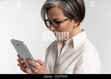 Close up. Senior grey haired woman in white shirt using digital tablet. The use of technology by the elderly browsing internet s Stock Photo