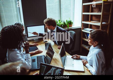 Young group of multi ethnic business people looking at computer with white screen at meeting. Supervisor of project showing info Stock Photo