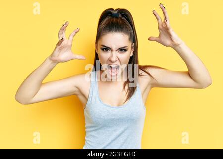 Screaming emotional angry young woman close up portrait over yellow background Stock Photo