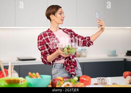 Woman in hair curlers taking funny selfie on mobile while cooking in the  kitchen Stock Photo - Alamy