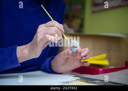 Happy elderly woman painting for fun at home. Senior Caucasian senior woman painting. Retirement hobby. Elderly woman painting o Stock Photo