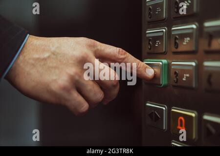 Close up of male hand presses button with braille for blind. Close up shot. Hand of office worker in business suit press the ele Stock Photo