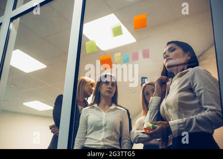 Young professional team. Group of young freelancers use sticker papers posting on the glass wall working on ideas and communicat Stock Photo