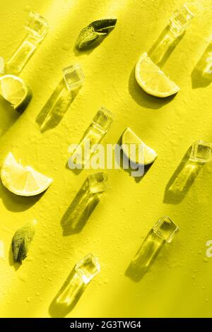Fresh mint leaf and ice cubes with droplets and lime on illuminating yellow  background Stock Photo