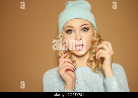 Gorgeous young woman with blond ringlets in a green knitted winter outfit ,over light brown Stock Photo