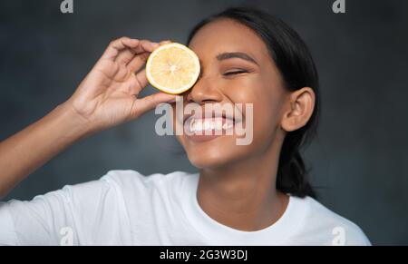 Portrait of beautiful young smiling woman holding lemon slice in front of eye Stock Photo