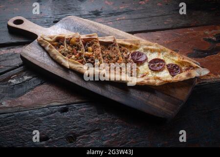 Turkish pide with sausage, beef and vegetables on rustic wooden table