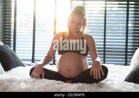 Pretty pregnant woman in black leggins and bra relaxing on her bed at home Stock Photo