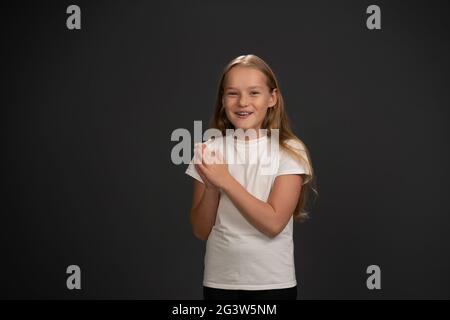 Excited little girl inspired by parents with hands put together happily looking at the camera wearing white t-shirt and black pa Stock Photo