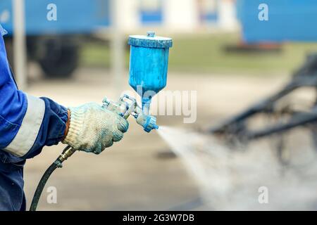 Spray gun in hand. A worker in overalls and a glove holds a spray compressor for painting in his hand. Stock Photo