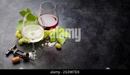 White and red wine glasses, grape, cork and vintage corkscrew on old stone table with copy space Stock Photo