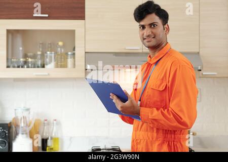 Portrait of content young Indian repairman in orange bodysuit making notes in clipboard while inspecting house Stock Photo