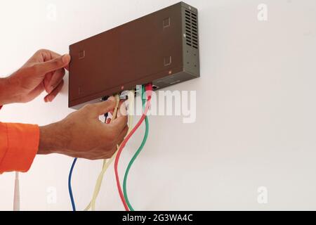 Close-up of unrecognizable black man connecting colorful wires into transmitter attached to wall Stock Photo
