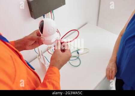 Close-up of unrecognizable man holding wired camera and installing at home under control of house owner Stock Photo