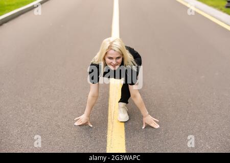 Sportive woman working out outdoors. Young lady doing exercises and ready to start running. Health and sport concept. Stock Photo