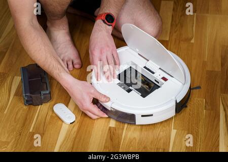 Housework and technology concept. Maintenance and service of robot vacuum cleaner. Cleaning, repair, replacement of parts. Man r Stock Photo