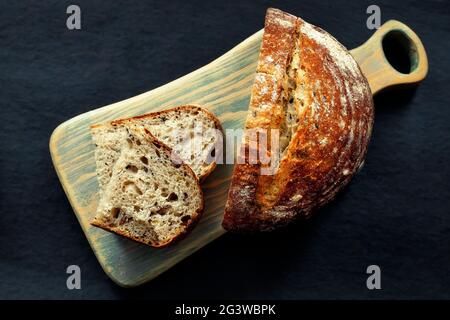 Fresh homemade bread lies on a cutting board on a dark background. Crunchy French sourdough bread. Fresh baked goods with cereal Stock Photo