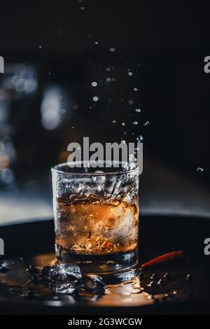 Ice cubes fall into a glass - whiskey with ice in a shot. Bar cocktail whiskey and cola. Cold ice in a glass of whiskey. Stock Photo