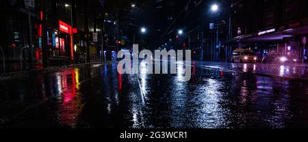 An empty rainy city street at night with lights reflecting in puddles in Melbourne Stock Photo