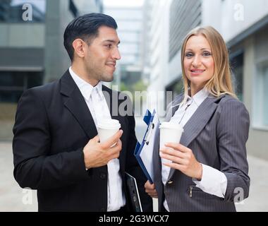 Businessman and his woman colleague in suit are standing with folder and coffee Stock Photo