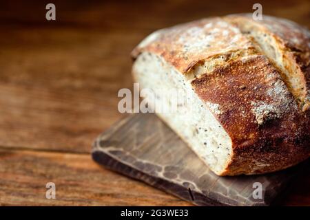 A round loaf of whole-grain homemade bread without yeast lies on a wooden board. Fresh pastries for a healthy diet. Stock Photo