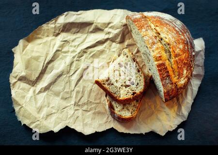 This is a loaf of fresh crusty bread with cereals on sourdough. Yeast-free homemade cakes lie on yellow craft paper. Stock Photo
