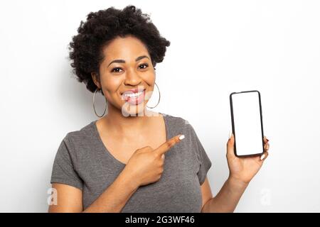 African woman shows her finger at the white screen of the smartphone. Black female holds a mobile phone. Stock Photo