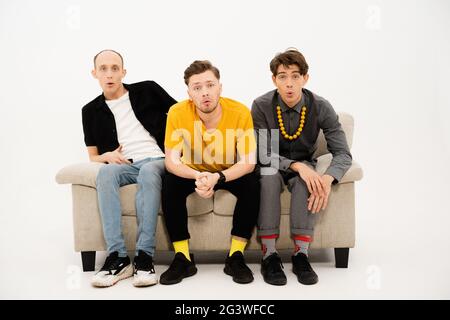 Portrait of three young friends spend time together sitting on the small sofa looking at the camera isolated on white background Stock Photo