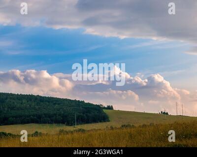 Massive clouds - towering cumulus - forming in the blue sky behind hilly landscape on the horizon Stock Photo