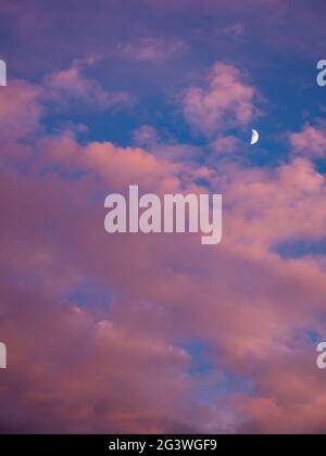 Crescent moon in a cloudy sky with red color clouds at sunset Stock Photo