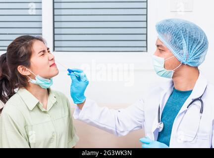 Coronavirus test, Doctor man take saliva sample through nose with cotton swab to check coronavirus test from Asian young woman, Covid-19 pandemic outb Stock Photo