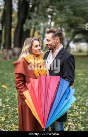 Looking in to the eyes of each other with closed rainbow umbrella beautiful in love couple standing in the park under a. A beaut Stock Photo
