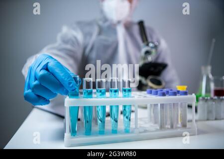 Biochemistry laboratory research, chemist in protective suit analyzing blue sample in laboratory with equipment, microscope and Stock Photo