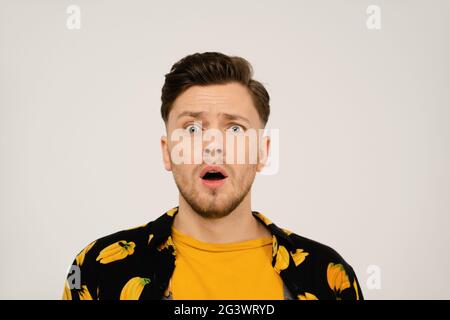 Surprised or shocked look on face of handsome man in dressed banana shirt and yellow t-shirt under looking at camera. Isolated o Stock Photo