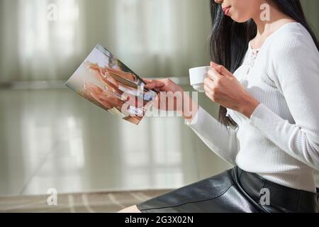 Close-up of content young Asian woman holding colorful photograph and drinking coffee while sitting on floor Stock Photo
