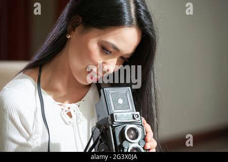 Satisfied attractive young Asian photographer with black hair looking through photos on old-fashioned camera Stock Photo